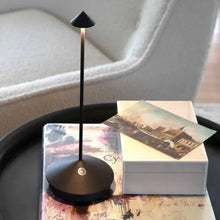Lade das Bild in den Galerie-Viewer, Schwarze LED-Tischlampe auf rundem Tisch, modernes Design, neben weißer Box und Postkarte.
