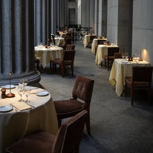 Lade das Bild in den Galerie-Viewer, Elegantes Restaurant mit gedeckten Tischen, braunen Stühlen und Kerzenlicht, ideal für Abendessen.
