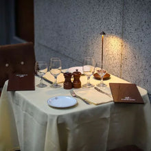 Lade das Bild in den Galerie-Viewer, Eleganter Restauranttisch mit Weingläsern, Speisekarten und Tischlampe, ideal für romantisches Dinner.
