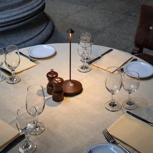 Runder Esstisch mit Tischlampe, Weingläsern, Pfefferstreuer und Servietten in elegantem Ambiente.